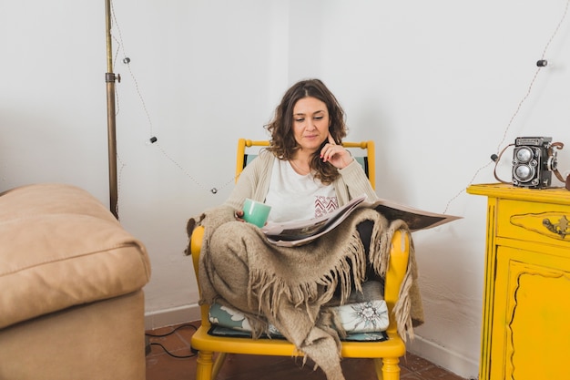 Free photo concentrated woman reading newspaper sitting on a chair