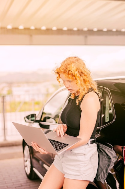 Free Photo concentrated woman working on laptop beside car