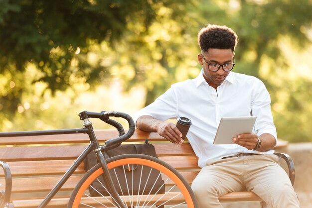 Concentrated young african man using tablet drinking coffee.