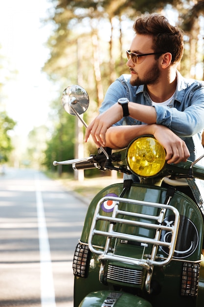 Concentrated young bearded man sitting on scooter outdoors