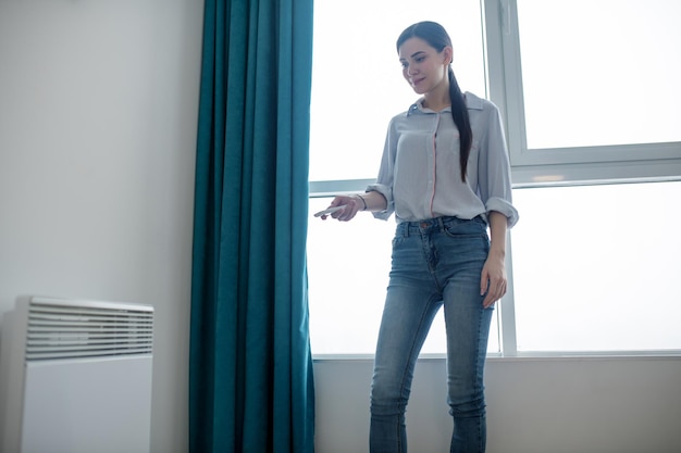 Free Photo concentrated young beautiful dark-haired caucasian woman using a remote controller for heating a living room