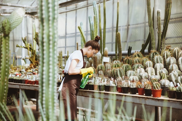 Concentrated young lady in glasses standing in greenhouse