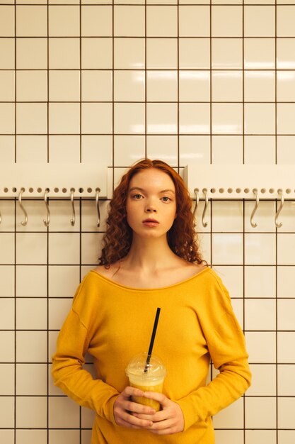 Concentrated young redhead curly lady standing in cafe