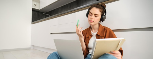 Free photo concentrated young student woman working on assignment doing homework on laptop making notes in