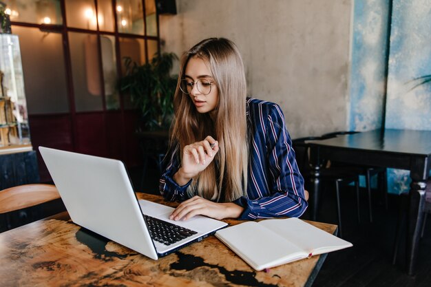 Concentrated young woman working in favorite cafe. Indoor shot of charming serious female student using laptop.