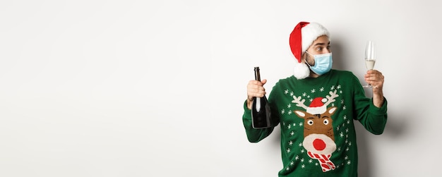 Free photo concept of covid and christmas holidays man in medical mask and santa hat enjoying glass of champagn