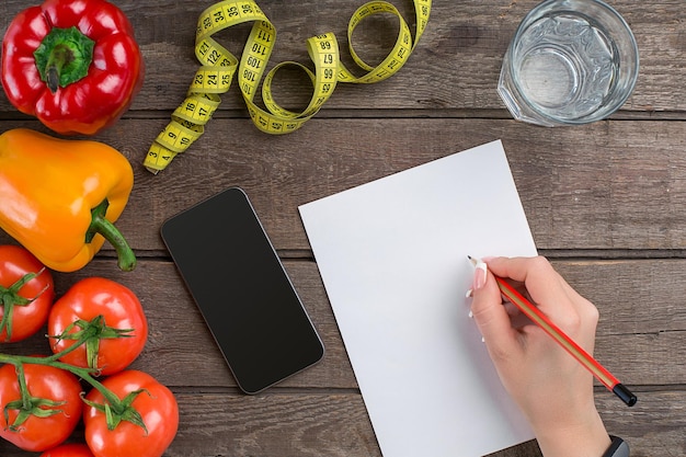 Free photo concept diet, slimming plan with vegetables top view mock up. a female hand in a sports bracelet writes an article about proper nutrition