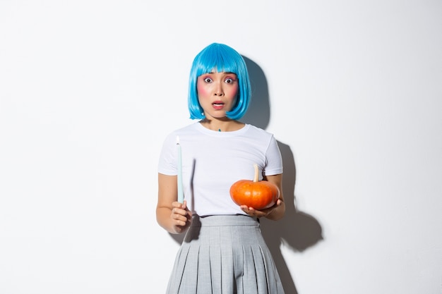 Free Photo concept of halloween. image of scared asian girl in blue wig looking nervous and frightened, holding candle and pumpkin.