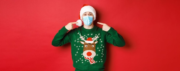 Concept of new year coronavirus and social distancing happy man in santa hat and christmas sweater r...