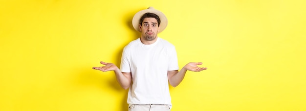 Free photo concept of tourism and summer confused male tourist shrugging looking indecisive standing against ye