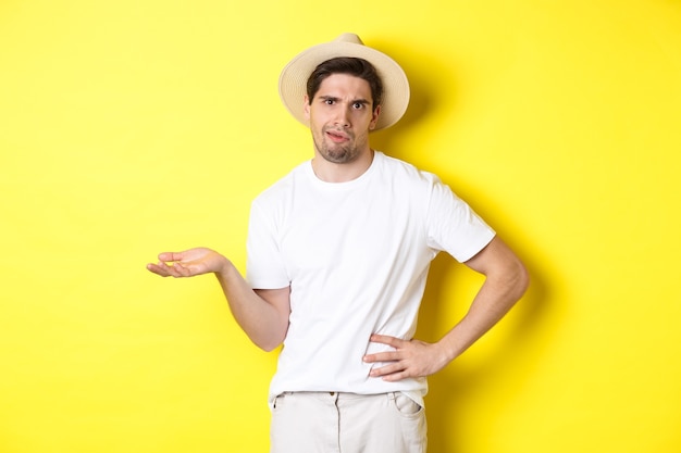 Concept of tourism and summer. Young skeptical tourist complaining, looking judgemental, standing over yellow background.