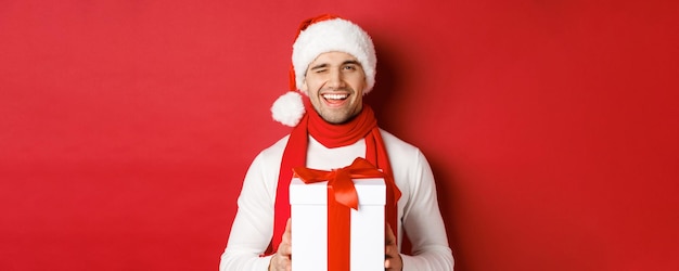 Free photo concept of winter holidays christmas and lifestyle handsome cheeky man in santa hat and scarf holdin