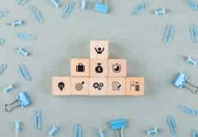 Free photo conceptual of business office with wooden blocks with icons, paperclips, binder clips top view.