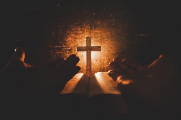 conceptual image focus on candle light with man hand holding wooden cross on bible and blurred world