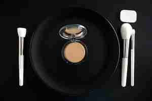 Free photo conceptual image of make up brushes next to dinner plate on black background