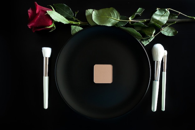 Free photo conceptual image of make up brushes next to dinner plate on black background