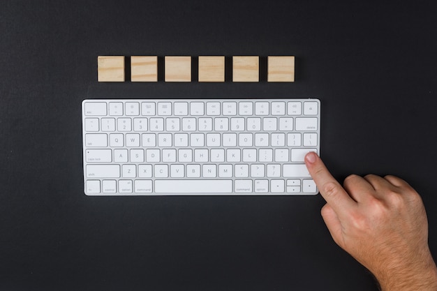 Conceptual of research man hitting enter key. with keyboard, wooden cubes on black desk background flat lay. horizontal image