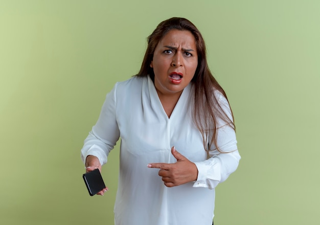 Concerned casual caucasian middle-aged woman holding and points at phone 