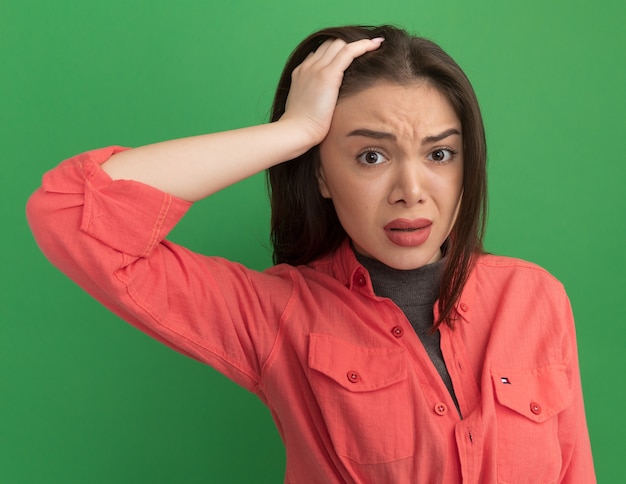 Concerned young pretty woman putting hand on head looking at front isolated on green wall