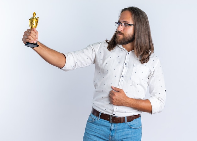 Free Photo confident adult handsome man wearing glasses keeping hand on belly stretching out and looking at winner cup isolated on white wall