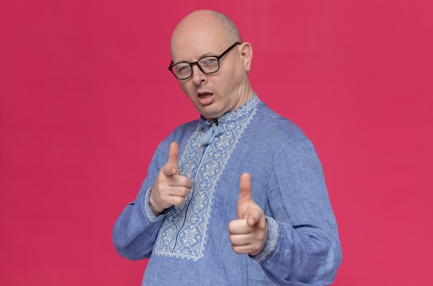 Confident adult man in blue shirt wearing glasses blinking his eye and pointing at front