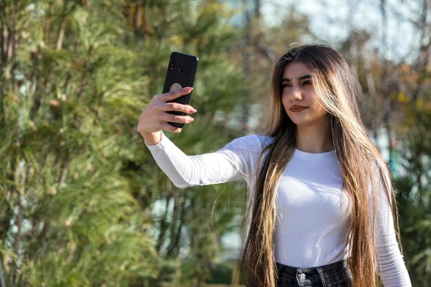 Confident beautiful girl taking selfie at the park on sunny day High quality photo