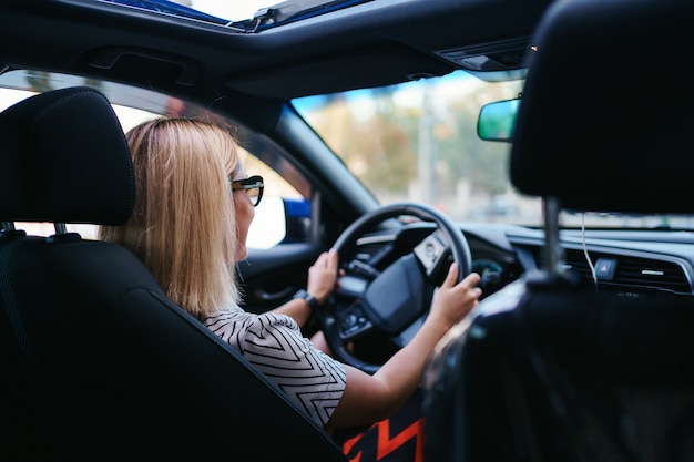 Free photo confident and beautiful woman in sunglasses. rear view of attractive young female in casual wear driving a car