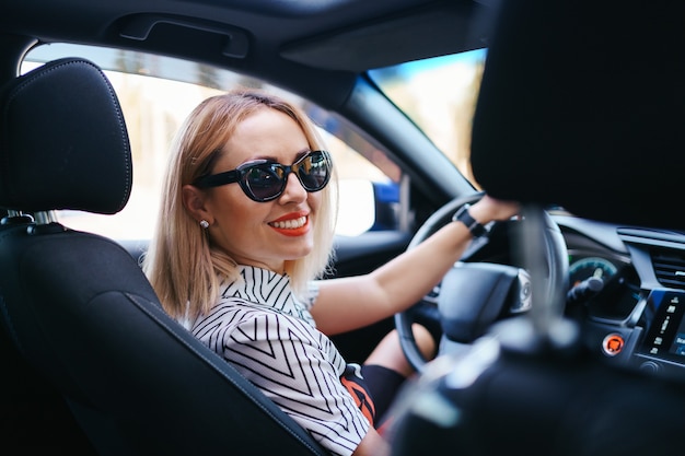 Free photo confident and beautiful woman in sunglasses. rear view of attractive young female in casual wear driving a car