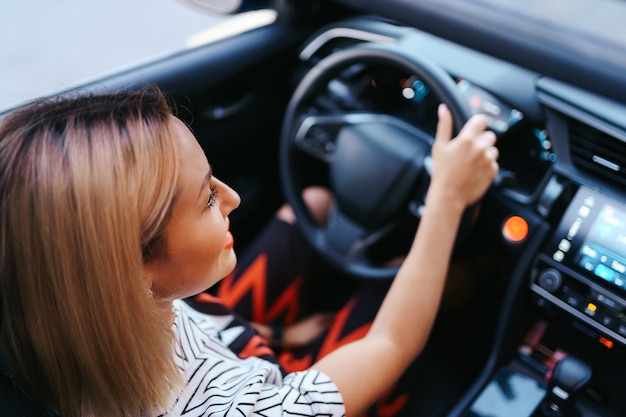 Confident and beautiful woman in sunglasses. Rear view of attractive young female in casual wear driving a car