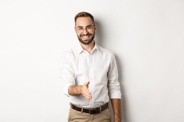 Confident businessman extending hand for handshake, greeting business partner and smiling, standing