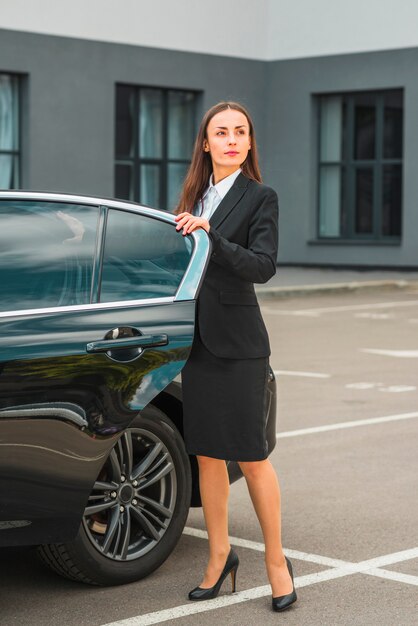 Confident businesswoman standing near open car door