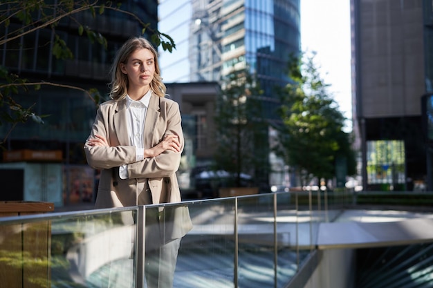 Free photo confident businesswoman in suit holds hands crossed on chest stands in power pose on street