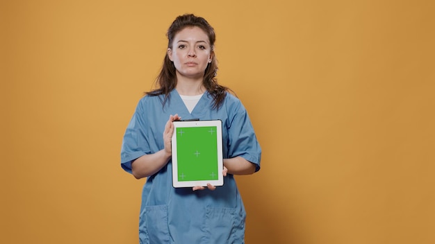 Free photo confident caucasion doctor posing holding digital tablet with green screen mockup design wearing hospital uniform in studio. woman medic using touchscreen device for advertising medical concept.