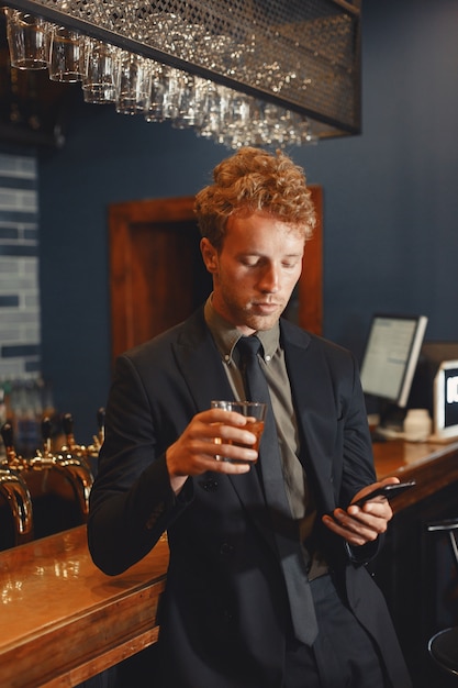 Free photo confident cheerful man sitting at bar counter, drinking beer and networking on smartphone.