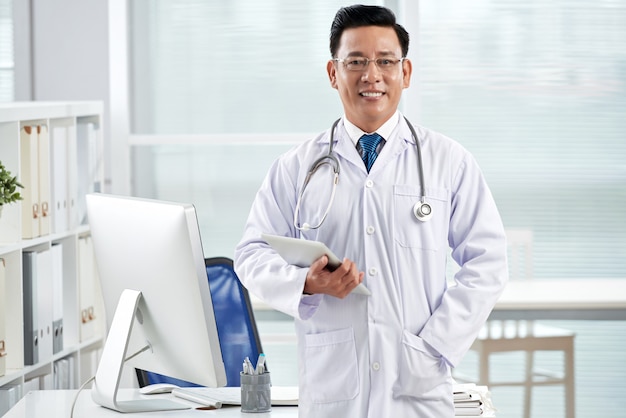 Confident doctor looking at camera holding the tablet PC