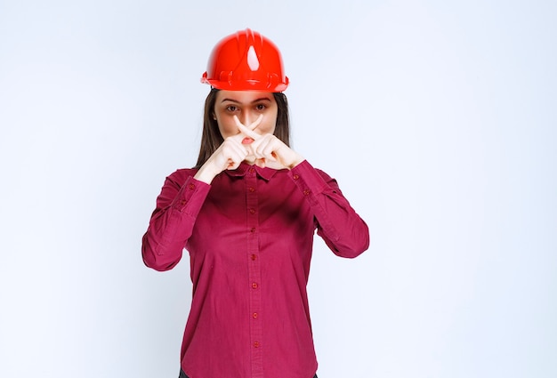 Free photo confident female architect in red hard helmet showing stop sign.