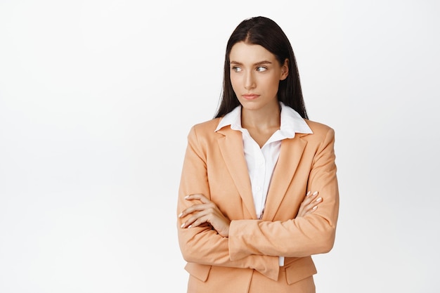 Confident female entrepreneur cross arms on chest looking left with serious strong face expression standing in suit against white background