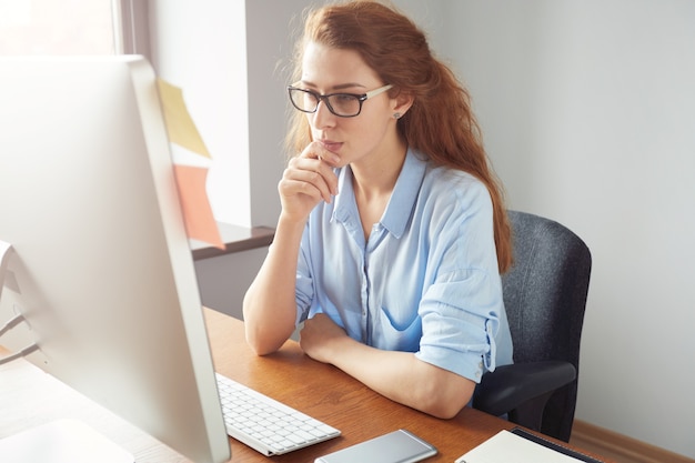 Confident female freelancer sitting in front of the computer with serious and thoughtful expression