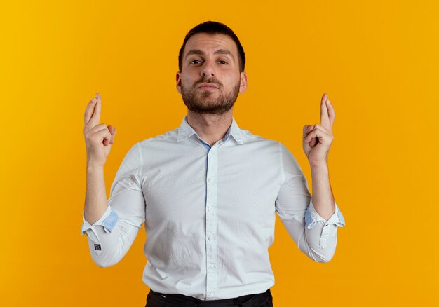 Confident handsome man crosses fingers isolated on orange wall