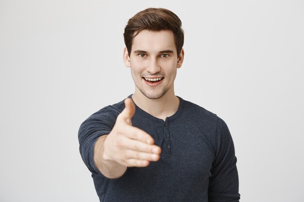 Confident handsome man extending his hand for handshake and smiling determined