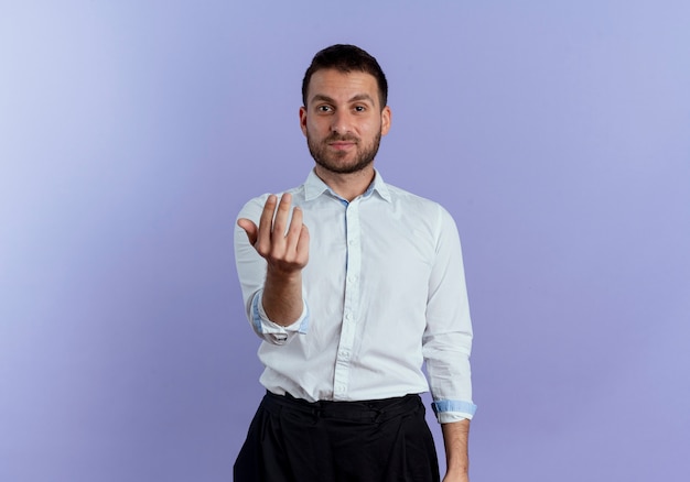 Confident handsome man gestures come here hand sign isolated on purple wall