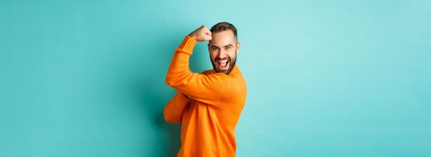 Confident handsome man showoff his muscles flex biceps feeling strong standing over light blue backg