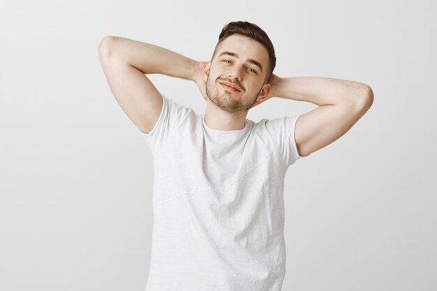 Free photo confident happy handsome man holding hands behind head and smiling pleased