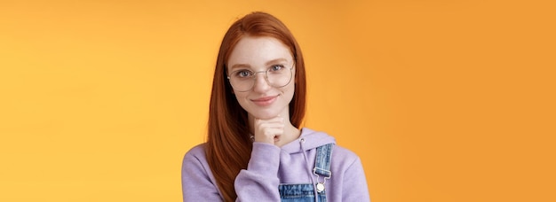 Free Photo confident happy relaxed european redhead skillful young female entrepreneur glasses establish startup smiling delighted look pleased result touch chin thoughtful smart orange background