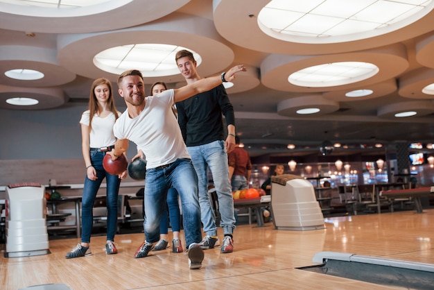 Confident in his own strenght. Young cheerful friends have fun in bowling club at their weekends