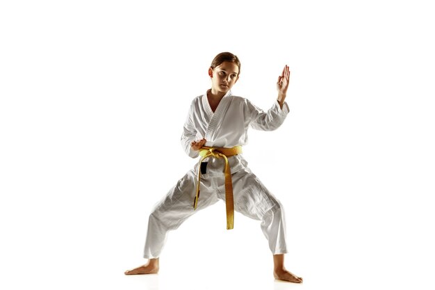 Confident junior in kimono practicing hand-to-hand combat, martial arts. Young female fighter with yellow belt s training on white  wall. Concept of healthy lifestyle, sport, action.