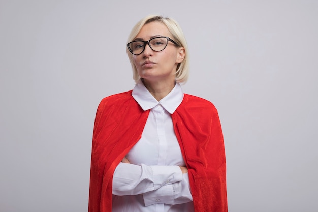 Free photo confident middle-aged blonde superhero woman in red cape wearing glasses standing with closed posture  isolated on white wall with copy space