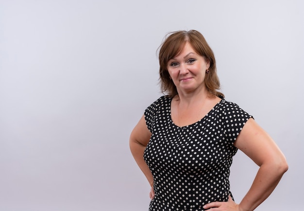 Confident middle-aged woman putting hands on waist on isolated white wall with copy space