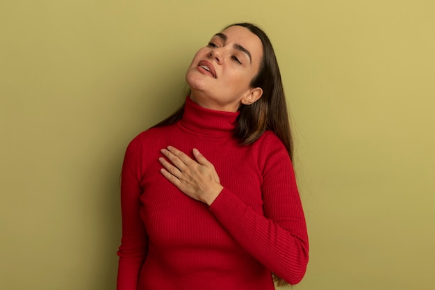 Confident pretty caucasian woman  hand on chest and looks at side on olive green