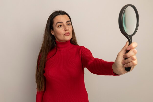 Confident pretty caucasian woman holds and looks at magnifying glass isolated